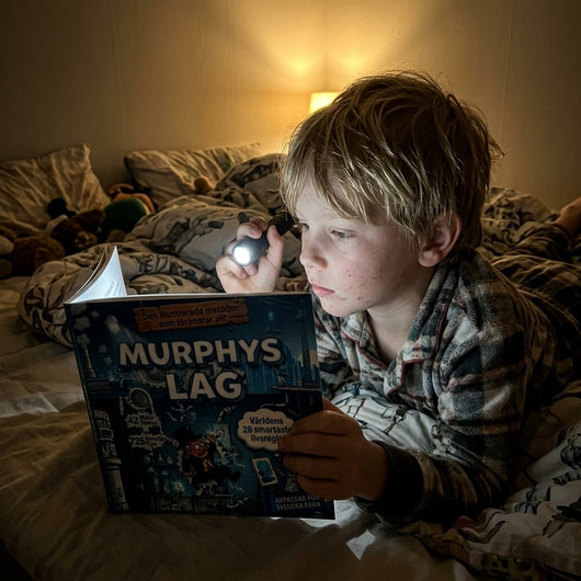 Pojke läser Murphys lag med ficklampa i sängen